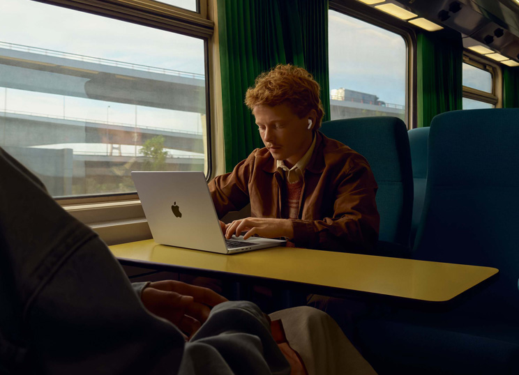 Iemand met AirPods die werkt op MacBook in een trein op een stoel bij het raam.