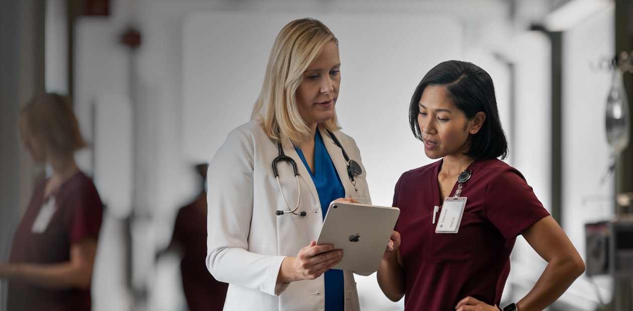 En læge og en sygeplejerske står på en hospitalsgang og kigger sammen på en iPad.