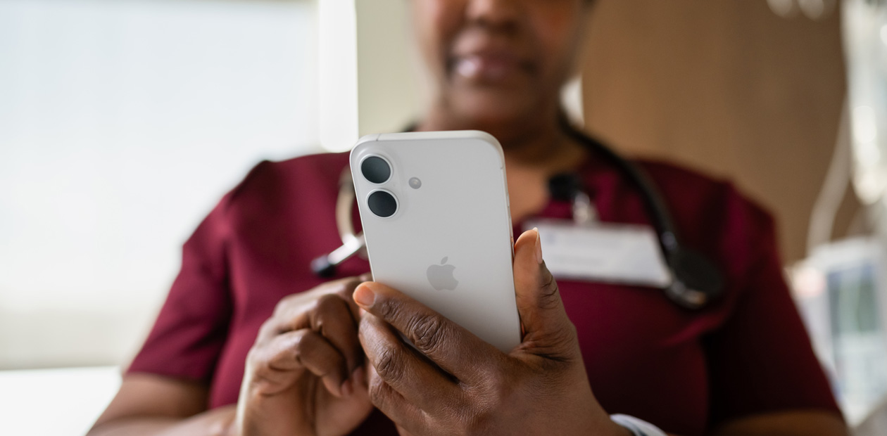 Eine weibliche Pflegekraft in rotem Kittel schaut auf ihr iPhone.